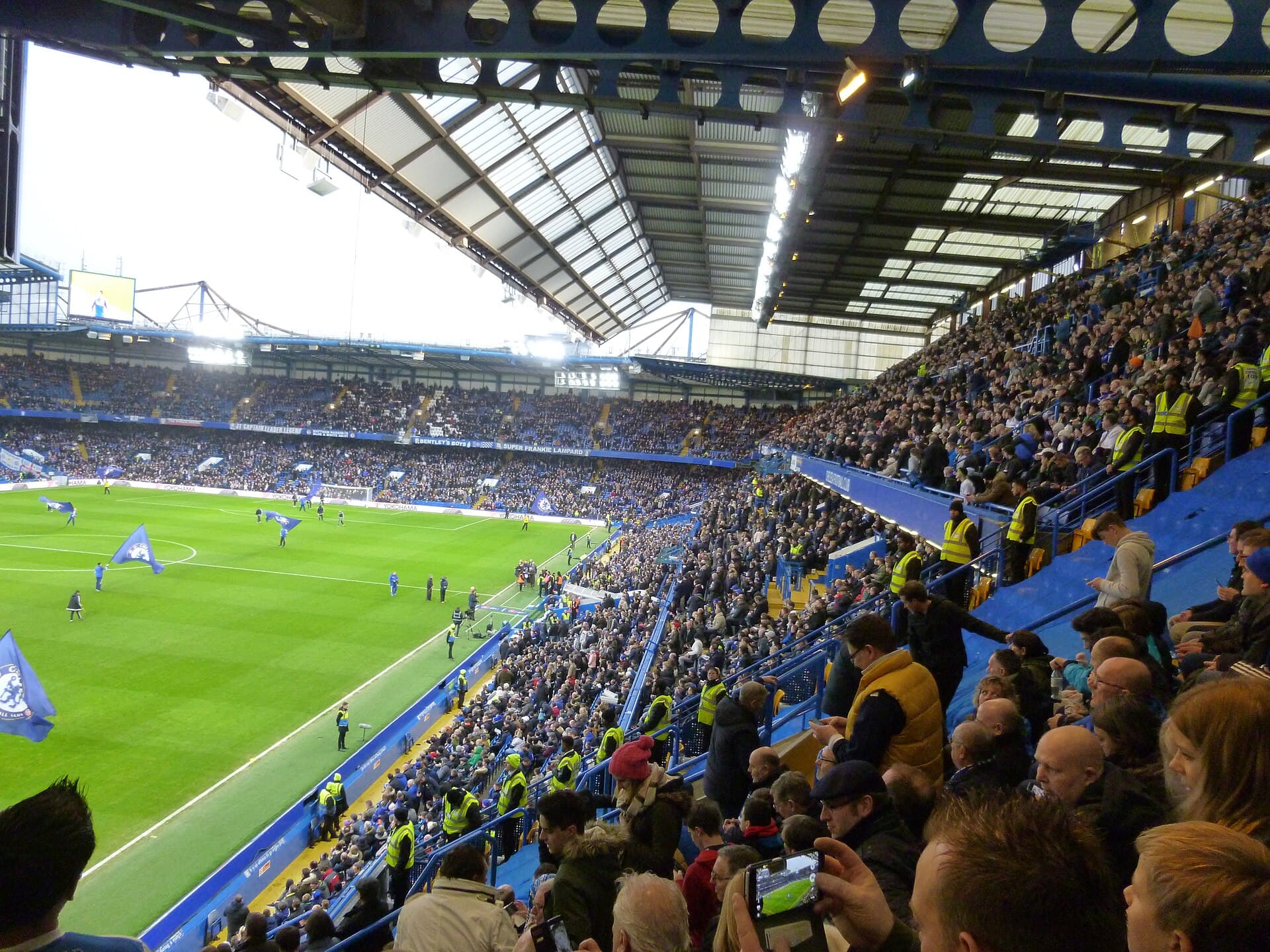 O Stamford Bridge cheio num Chelsea contra Peterborough, em janeiro de 2017, visto do alto da arquibancada lateral com o gramado à esquerda.