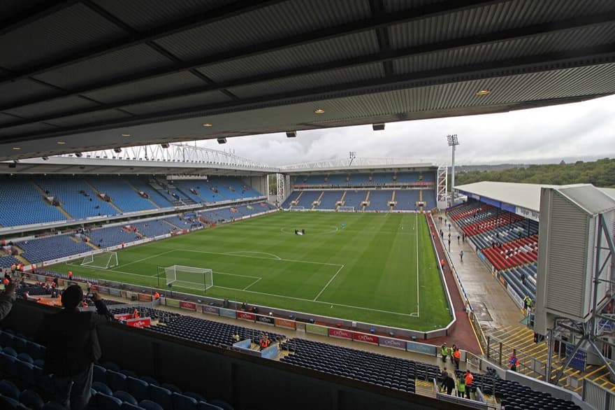 Ewood Park visto da arquibancada superior em dia de céu fechado, com as cadeiras azuis vazias antes do jogo.
